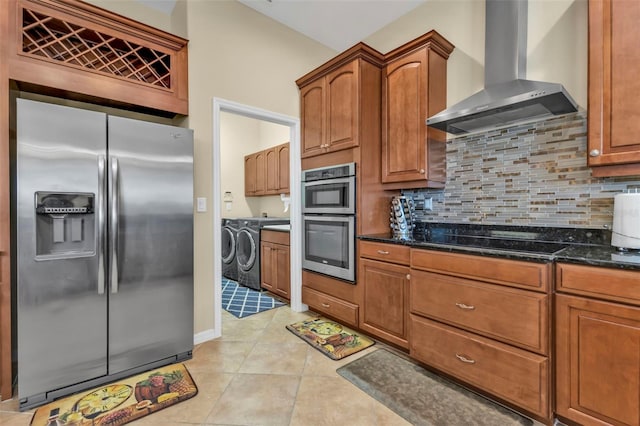 kitchen featuring brown cabinets, stainless steel appliances, decorative backsplash, light tile patterned flooring, and wall chimney range hood