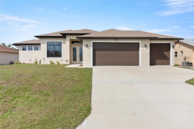 prairie-style house featuring french doors, stucco siding, a front yard, a garage, and driveway