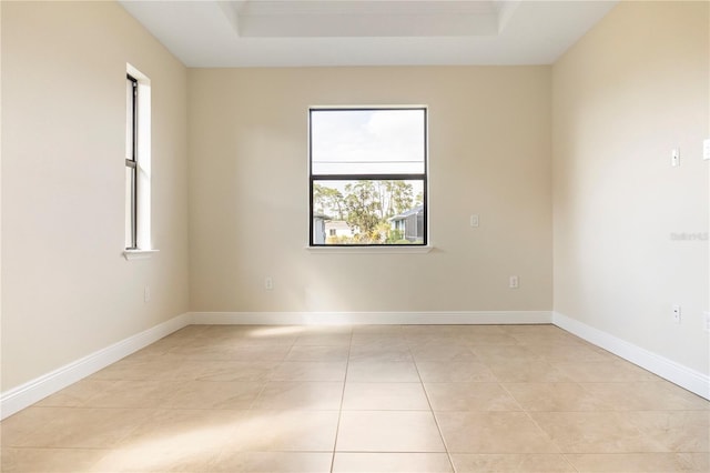 empty room featuring a tray ceiling, baseboards, and light tile patterned floors