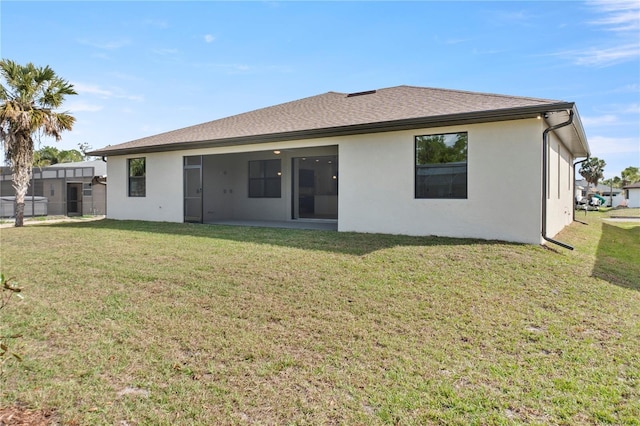 rear view of property featuring roof with shingles, a lawn, fence, and stucco siding