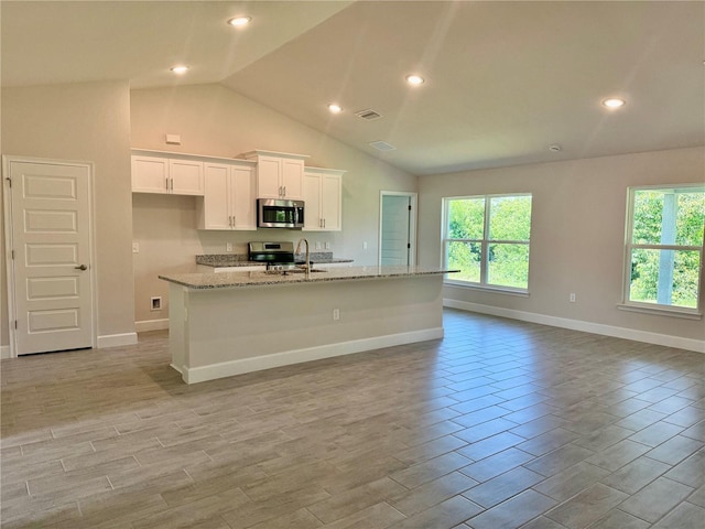 9590 Little Rock St, Port Charlotte, FL 33981 - kitchen featuring appliances with stainless steel finishes, healthy amount of natural light, white cabinetry, lofted ceiling, and an island with sink
