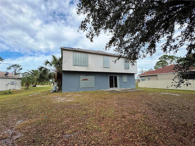 rear view of property featuring stucco siding, fence, and a yard