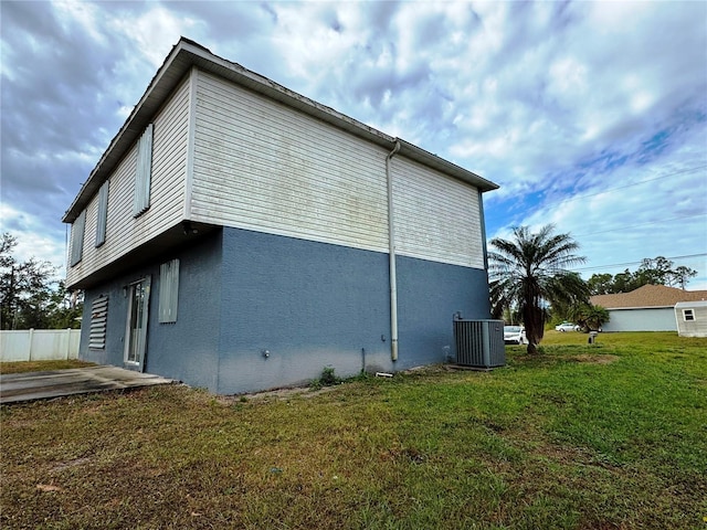 view of side of home featuring stucco siding, a yard, fence, and central AC unit