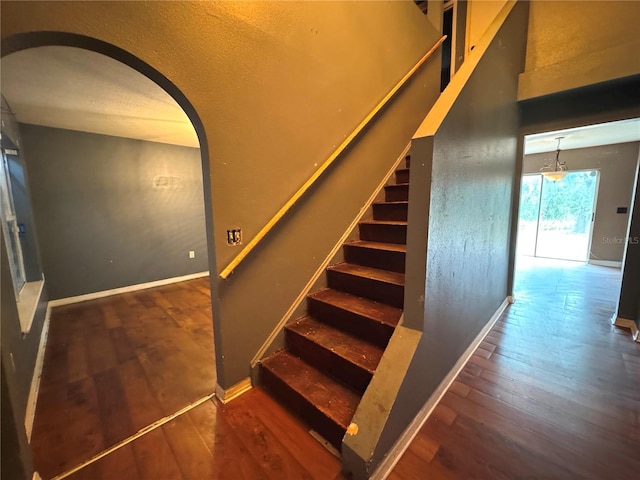 staircase with arched walkways, wood finished floors, and baseboards