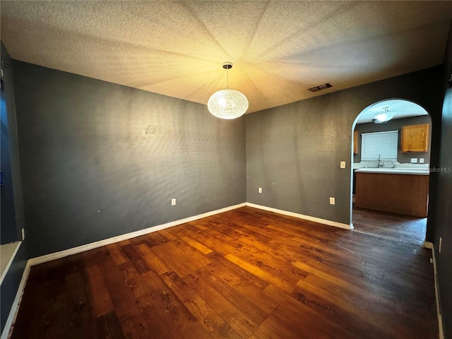 spare room with arched walkways, dark wood-style flooring, a textured ceiling, and baseboards