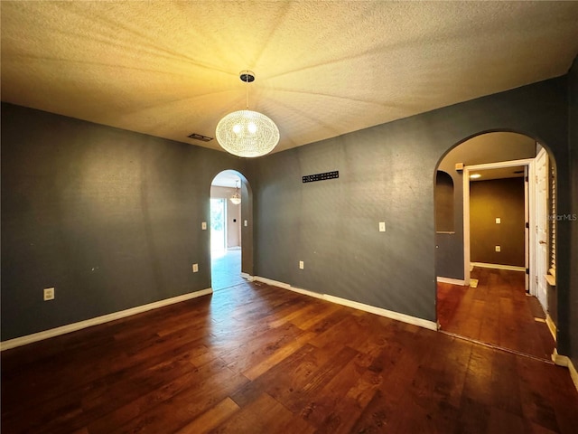 empty room with dark wood-style floors, arched walkways, a textured ceiling, and baseboards