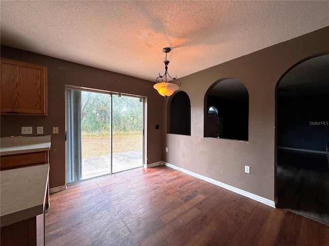 unfurnished dining area featuring a textured ceiling, baseboards, and dark wood-style flooring