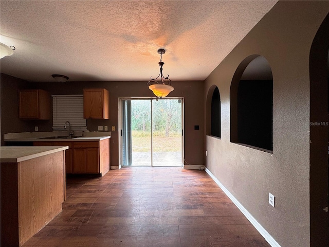 kitchen featuring brown cabinets, decorative light fixtures, light countertops, a textured wall, and a sink