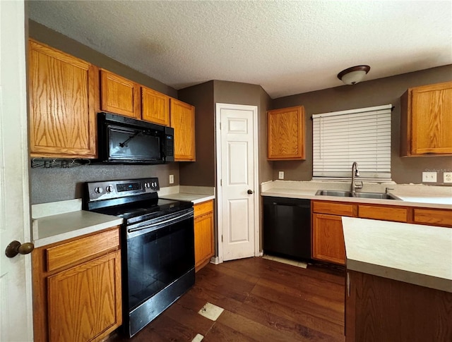 kitchen featuring dark wood-style floors, brown cabinets, light countertops, black appliances, and a sink