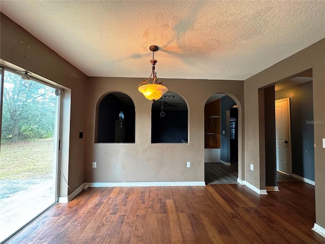 empty room with dark wood-style floors, baseboards, arched walkways, and a textured ceiling