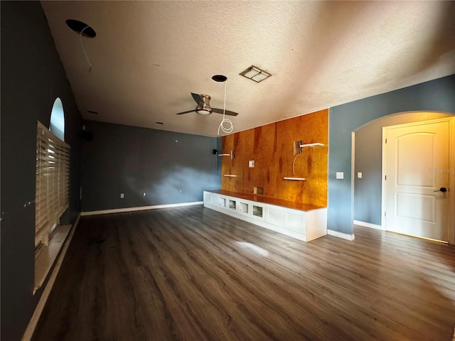 unfurnished living room with baseboards, arched walkways, visible vents, dark wood finished floors, and a textured ceiling