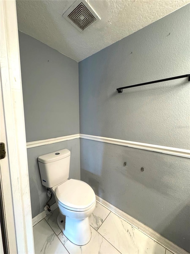 bathroom featuring baseboards, visible vents, toilet, marble finish floor, and a textured ceiling