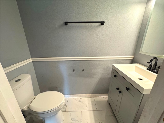 half bath with a textured wall, toilet, vanity, baseboards, and marble finish floor