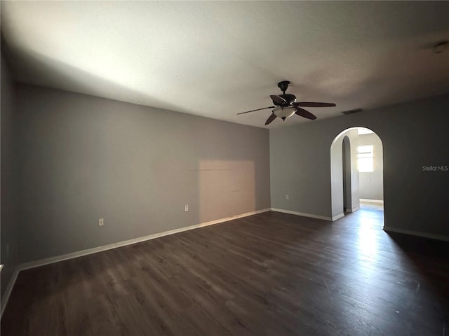 spare room featuring baseboards, visible vents, arched walkways, a ceiling fan, and dark wood-type flooring