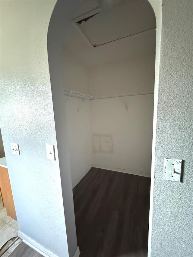 walk in closet featuring arched walkways and wood finished floors