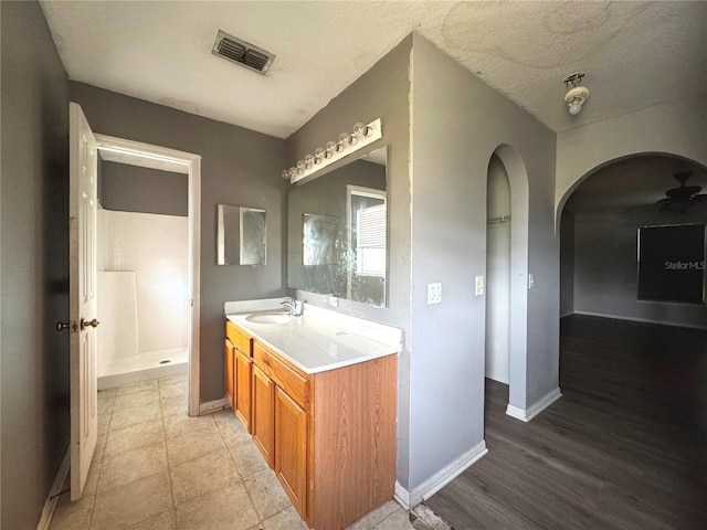 bathroom with a textured ceiling, vanity, baseboards, visible vents, and a shower stall