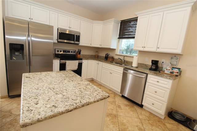 kitchen featuring appliances with stainless steel finishes, white cabinets, a kitchen island, a sink, and light stone countertops