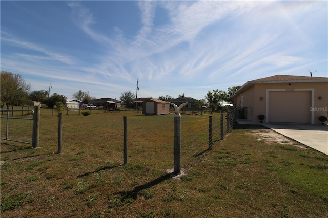 view of yard featuring an outbuilding, concrete driveway, a storage shed, an attached garage, and fence