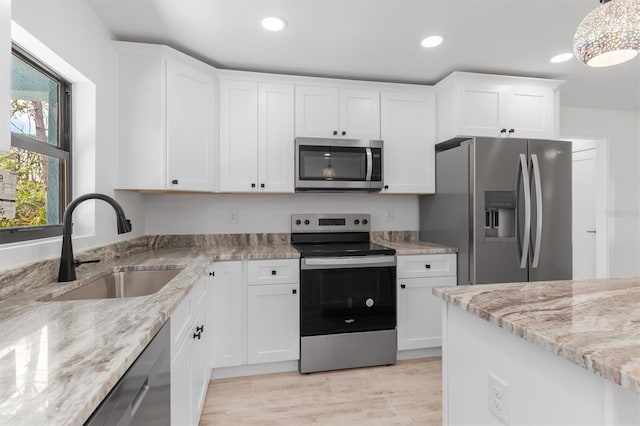 kitchen with light stone counters, a sink, white cabinetry, appliances with stainless steel finishes, and decorative light fixtures