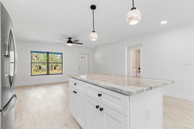 kitchen featuring stainless steel fridge, a kitchen island, light stone counters, open floor plan, and white cabinetry