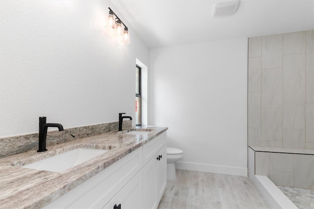 bathroom with wood finished floors, a sink, baseboards, and double vanity