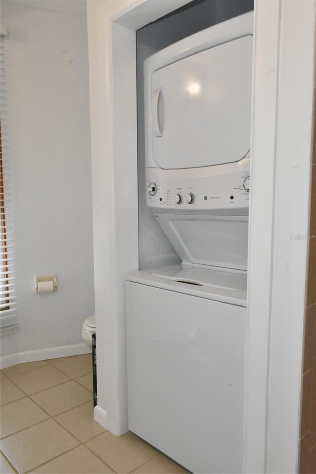 laundry area with light tile patterned floors, laundry area, stacked washer / dryer, and baseboards