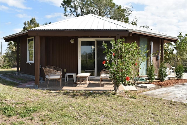 back of property with a standing seam roof, metal roof, a lawn, and a patio area