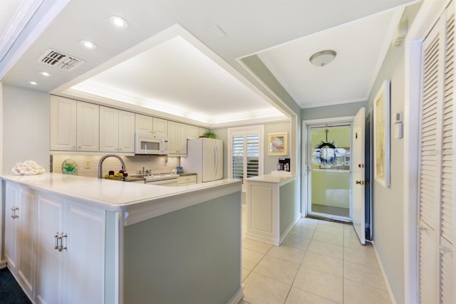 kitchen with a raised ceiling, light countertops, visible vents, white appliances, and a peninsula