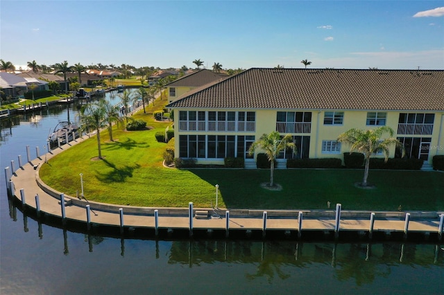 rear view of house with a water view, a tiled roof, a lawn, a residential view, and stucco siding