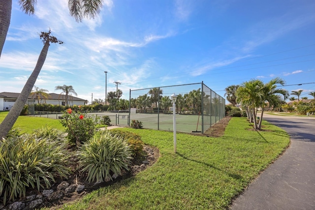 view of property's community featuring a gate, a tennis court, a lawn, and fence