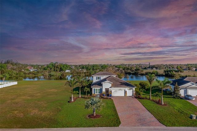 view of front of house with a garage, decorative driveway, a water view, and a yard