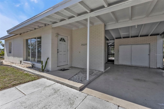 property entrance featuring an attached carport, brick siding, and driveway