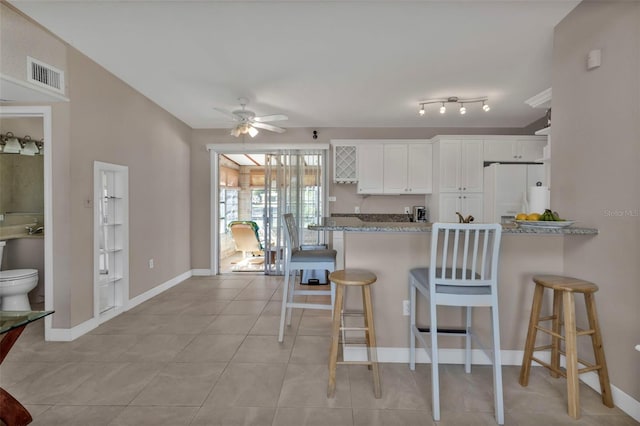 kitchen with visible vents, white cabinets, light stone countertops, white fridge with ice dispenser, and a kitchen breakfast bar