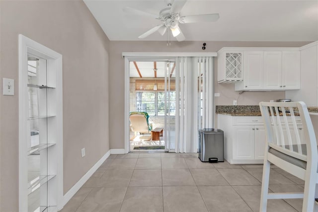 kitchen with a ceiling fan, white cabinetry, light tile patterned flooring, dark stone counters, and baseboards