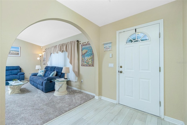 entryway featuring arched walkways, light wood-style flooring, and baseboards