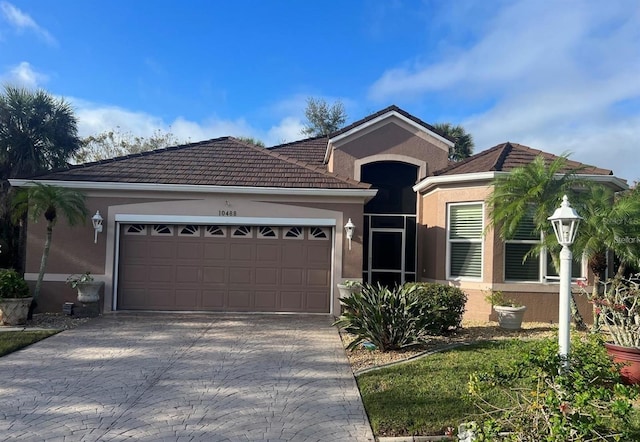 single story home with a garage, a tiled roof, decorative driveway, and stucco siding