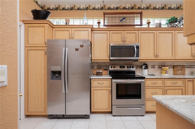 kitchen featuring light stone countertops, light tile patterned floors, appliances with stainless steel finishes, and light brown cabinetry