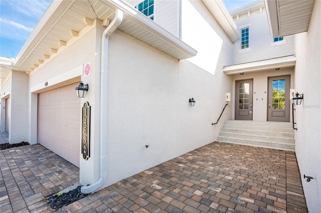 entrance to property featuring a garage and stucco siding