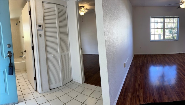 hallway featuring light tile patterned floors, a textured wall, and baseboards