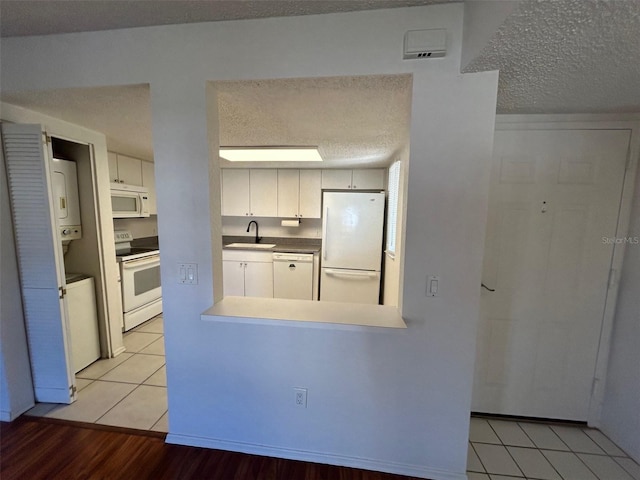 kitchen featuring white appliances, a textured ceiling, white cabinetry, a sink, and light tile patterned flooring