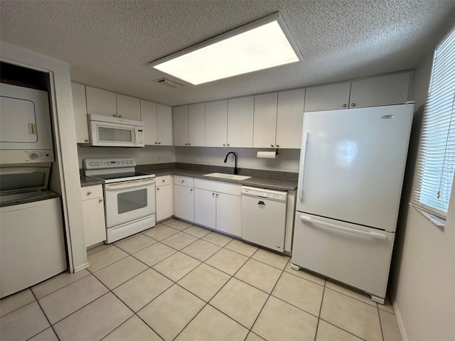 kitchen with white appliances, a sink, visible vents, stacked washer / drying machine, and dark countertops