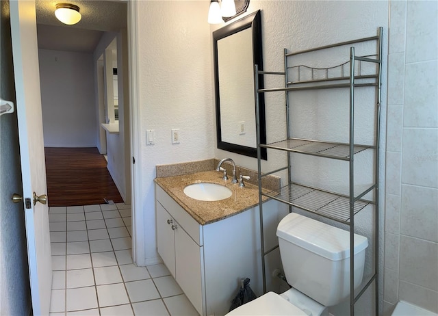 bathroom with tile patterned flooring, a textured wall, vanity, and toilet