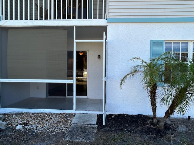 view of exterior entry featuring a balcony and stucco siding