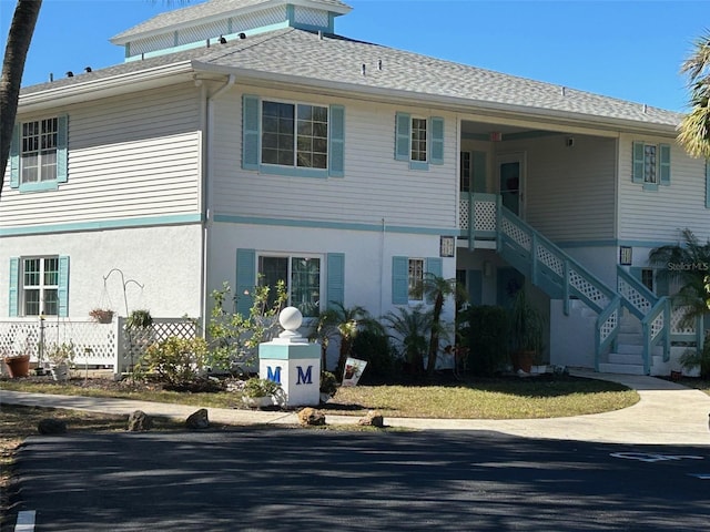 back of house with a shingled roof, stairs, and stucco siding