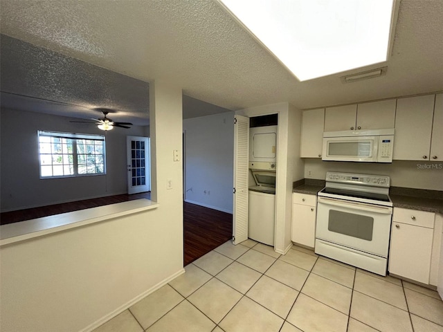 kitchen featuring light tile patterned floors, a textured ceiling, white appliances, stacked washer / drying machine, and dark countertops