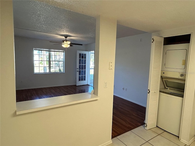 kitchen featuring a textured ceiling, ceiling fan, baseboards, stacked washer / drying machine, and tile patterned floors