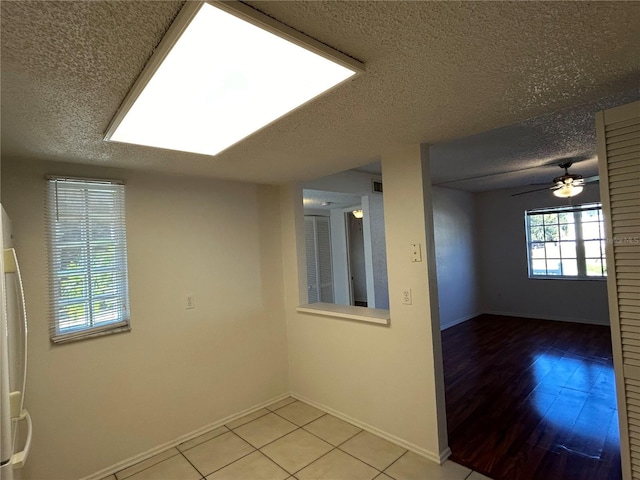 spare room featuring light tile patterned floors, visible vents, ceiling fan, a textured ceiling, and baseboards