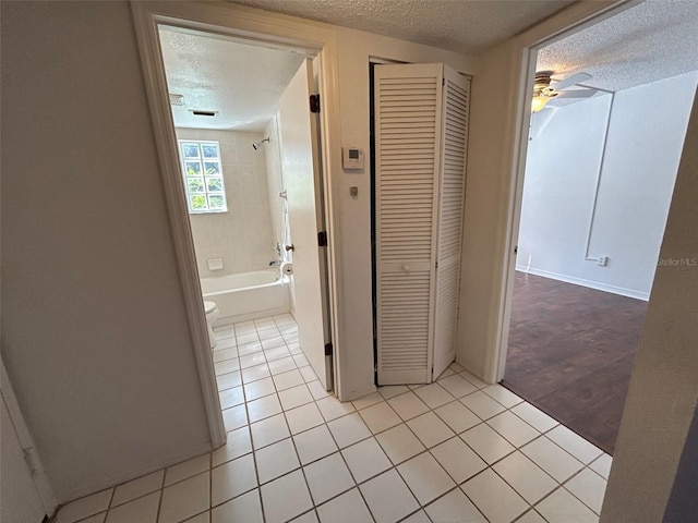 corridor with a textured ceiling, baseboards, and light tile patterned floors