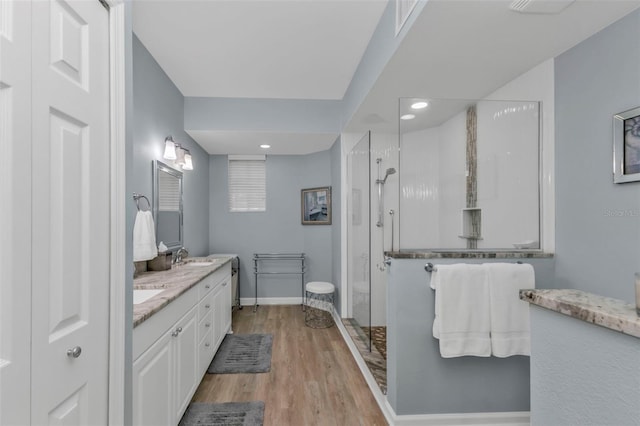 bathroom with a walk in shower, a sink, wood finished floors, baseboards, and double vanity