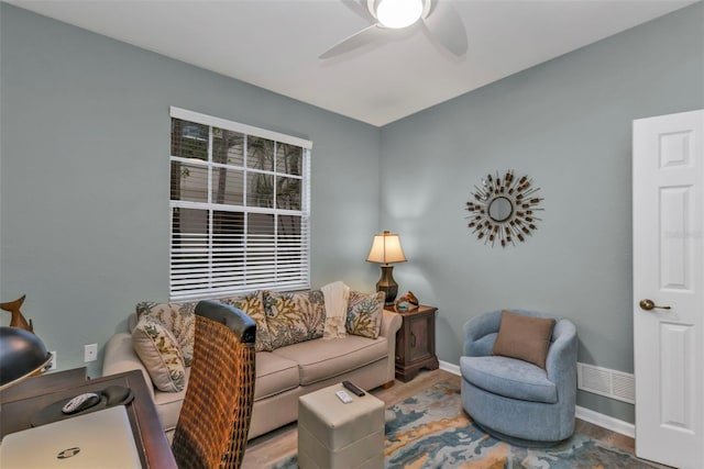 living area featuring visible vents, baseboards, a ceiling fan, and wood finished floors